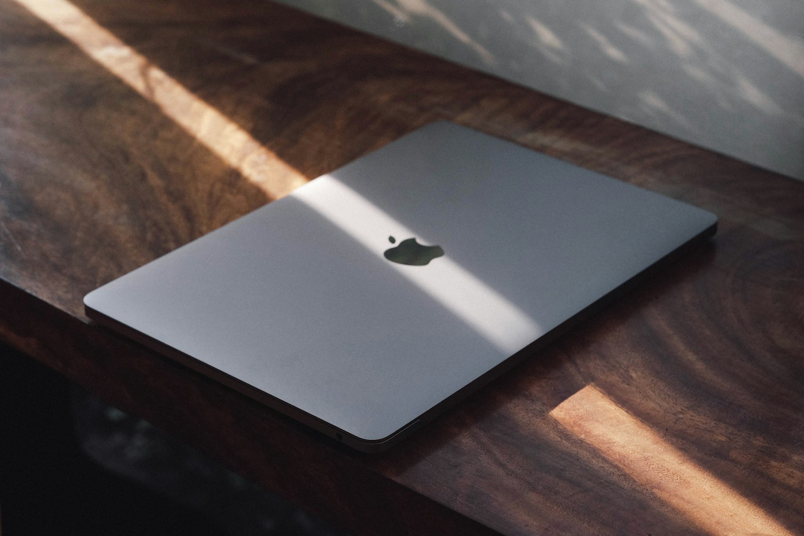 A closed MacBook resting on a wooden desk in afternoon sunlight